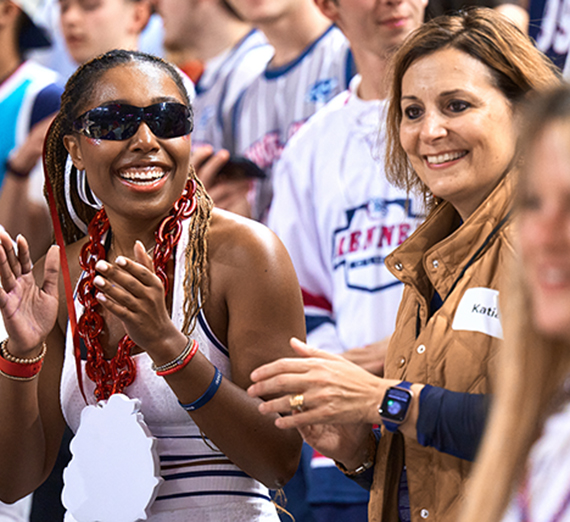 A woman in sunglasses claps in a crowd at a basketball game