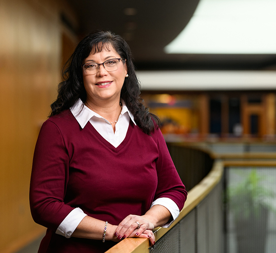 A women with dark hair wearing glasses and a red sweater leans on a bannister