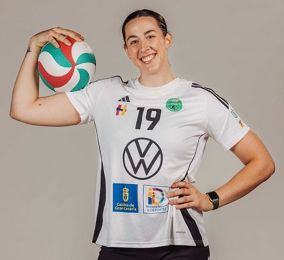 Female volleyball player wearing a white jersey with the number 19 and holding a green, white, and red volleyball. 