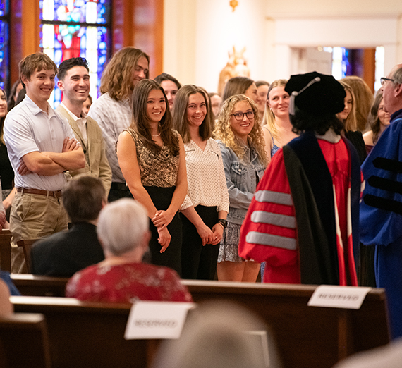 Two people in robes address a crowd of smiling students.