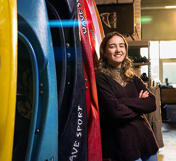 A woman stands next to several kayaks