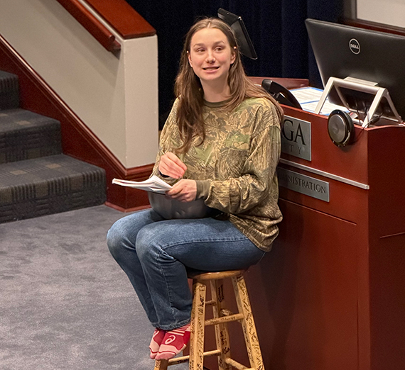 A woman sitting on a stool next to a podium