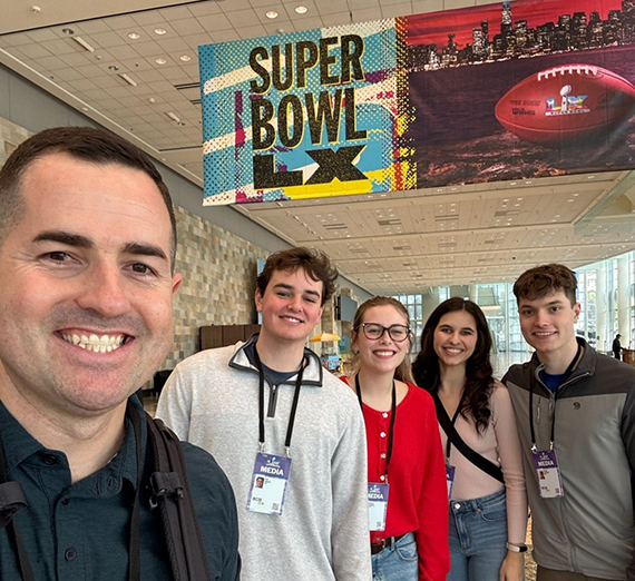 five people stand in front of a sign that says Super Bowl