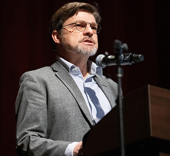 a bearded man speaks at a podium