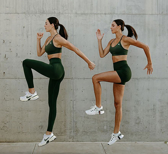 Two women in green exercise clothes raise their left leg in a running pose