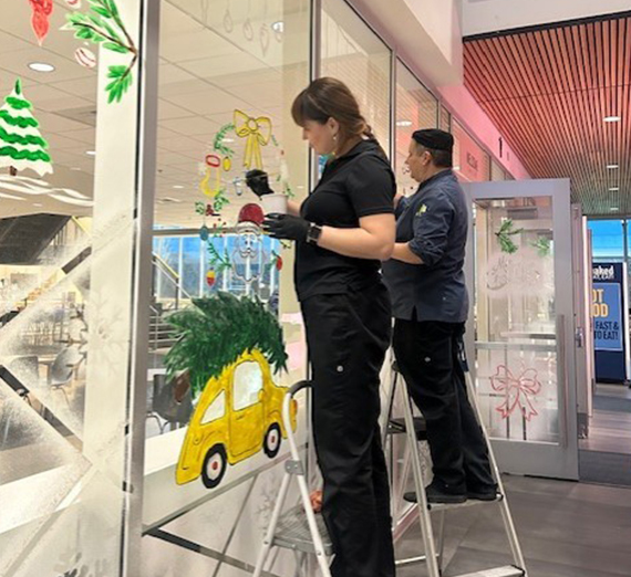 Two people painting art on a window.