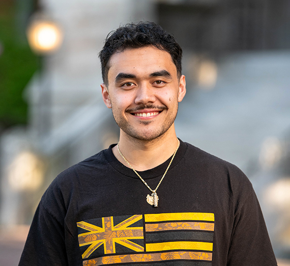 A main with a mustache wearing a brown t-shirt and necklace