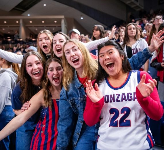 6 students smiling and cheering at a Gonzaga basketball game in the Kennel's student section.