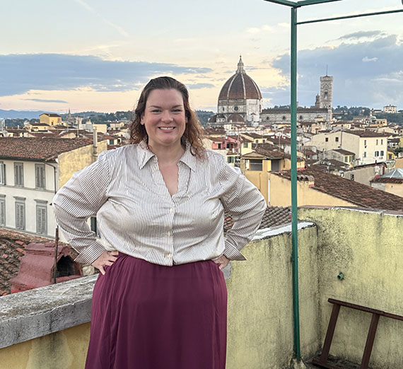 Woman wearing white button up and burgundy maxi skirt standing with views of Florence, Italy in the background
