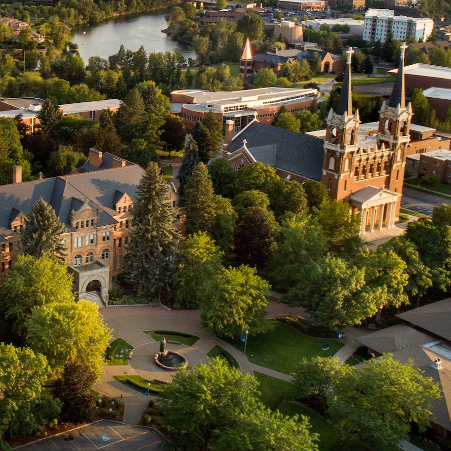 Drone view of campus with an overhead view of College Hall and St. Al's church with two white spires on top. In the background is the Spokane River.
