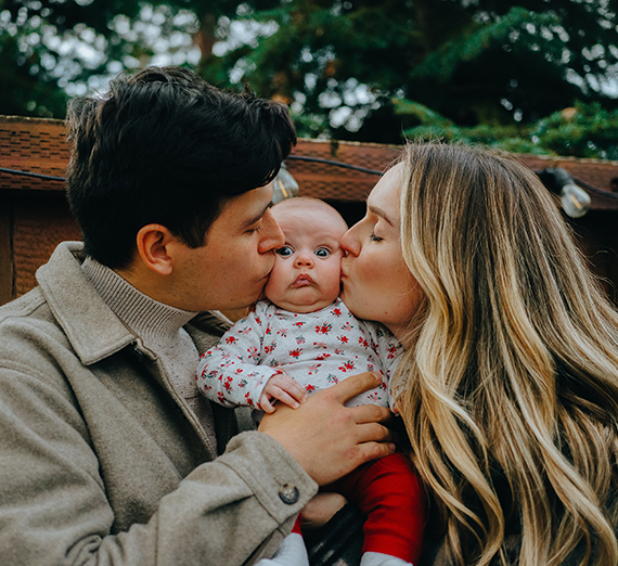 Mom and dad kissing a baby's cheek.