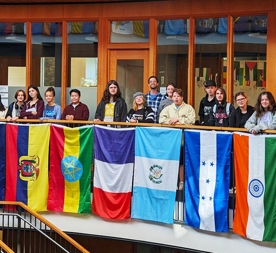 Wesley Schantz stands with students besides international flags in Gonzaga's Hemmingson Center. 