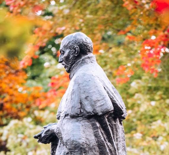 Profile view of the St. Ignatius statue in front of College Hall with fall leaves in the background.