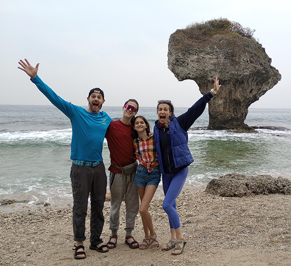 A family on a beach in front of a rock.