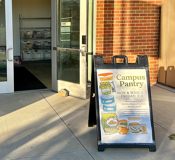 The Campus Pantry sign sits on the sidewalk outside an open door.