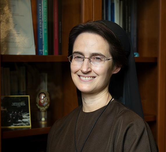 nun in brown habit in front of bookcase