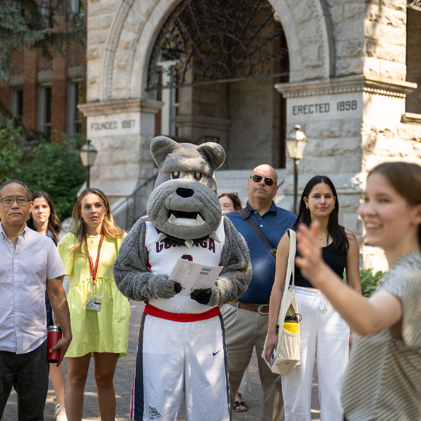 Image of a tour walking in front of College Hall with Spike holding a visit folder in the middle of the group.