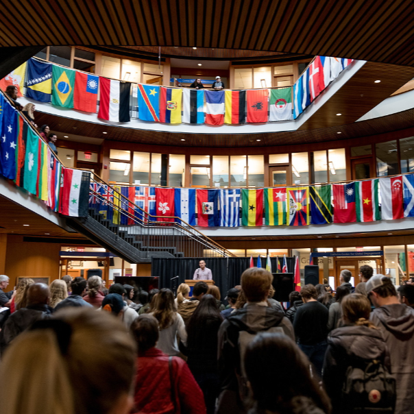 Crowd of students gathered in the Hemmingson Center Rotunda listening to a speaker. Hemmingson is decorated with different countries' flags each representing  a member of our campus community.