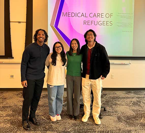 four UW-GU students pose in front of a presentation screen