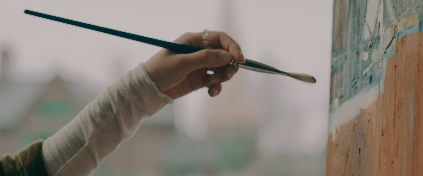 A student's hand holding a paint brush.