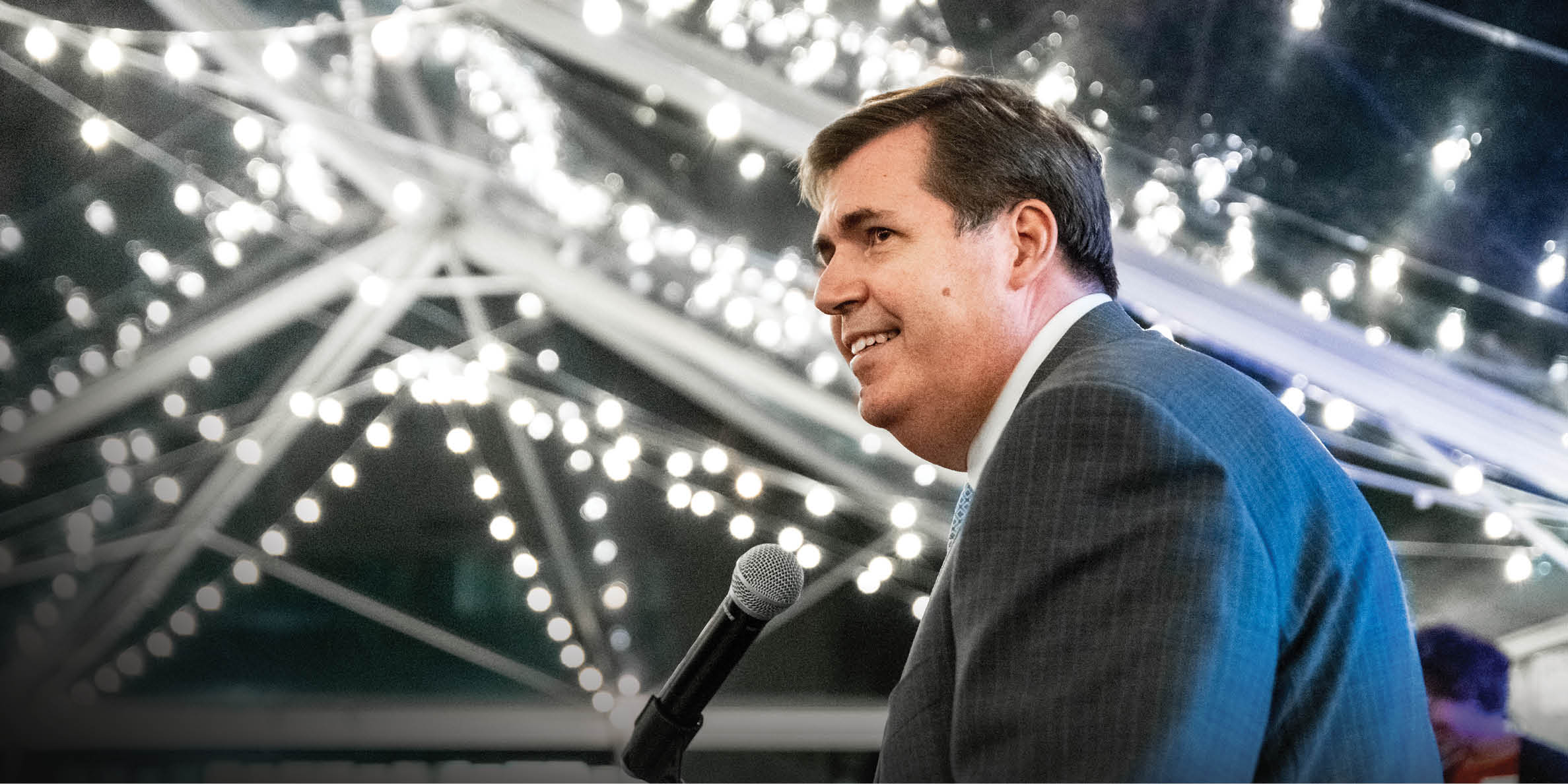 President Thayne McCulloh speaks at a microphone, with sparkling lights above him.