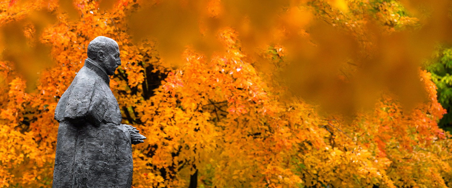 St. Ignatius statue on Gonzaga University campus against a backdrop of fall leaves.