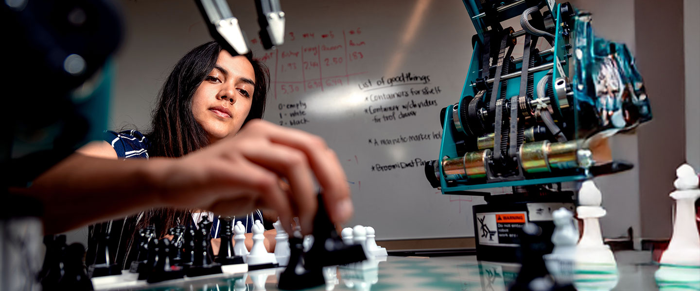 A student playing chess with a robot as the competitor in a classroom.