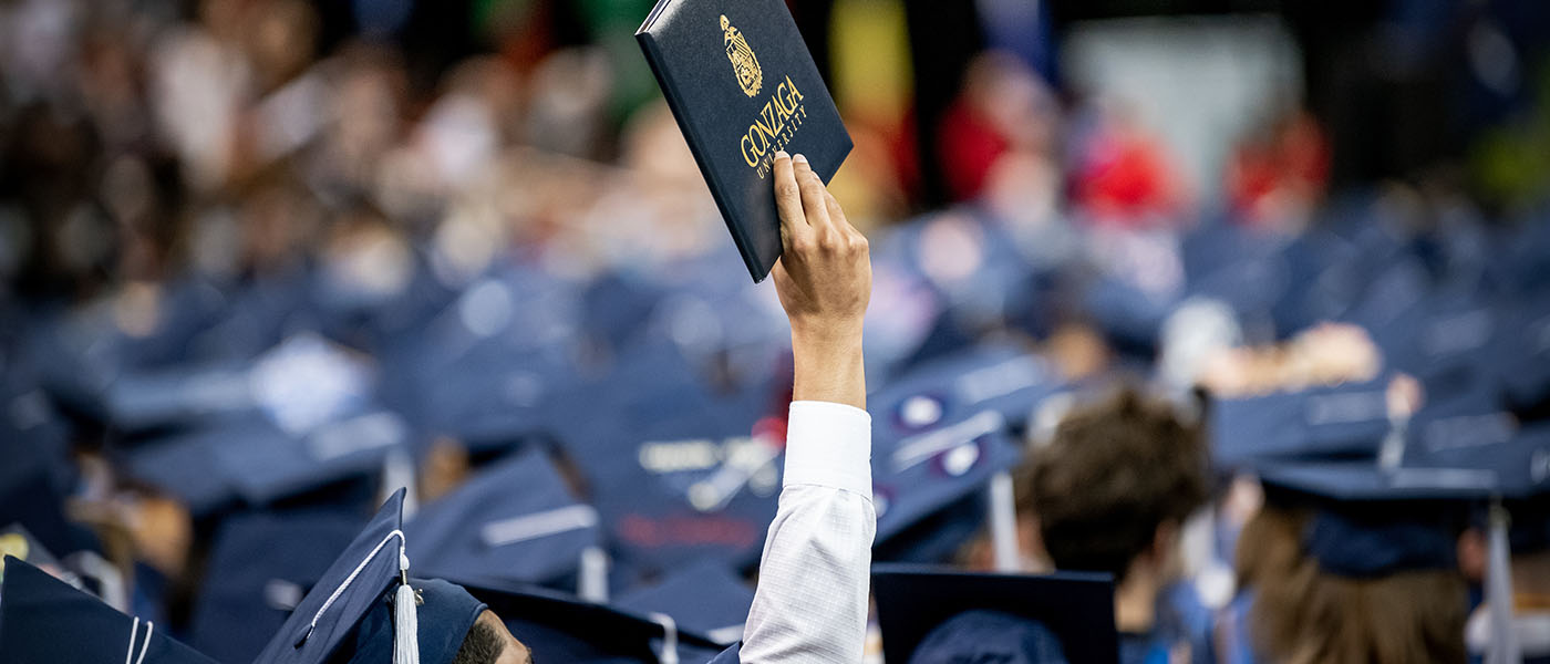 Arm raising graduation folio in graduation audience.